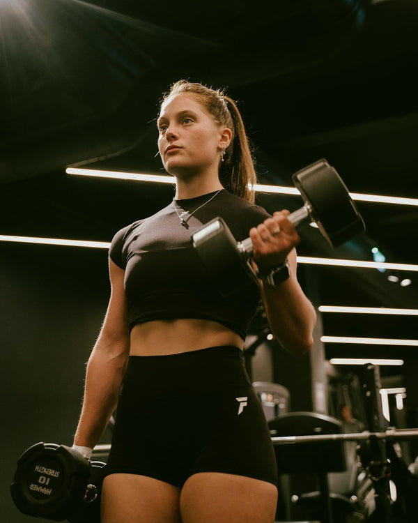 Vrouw in zwarte Frontline set met een dumbbell in de gym