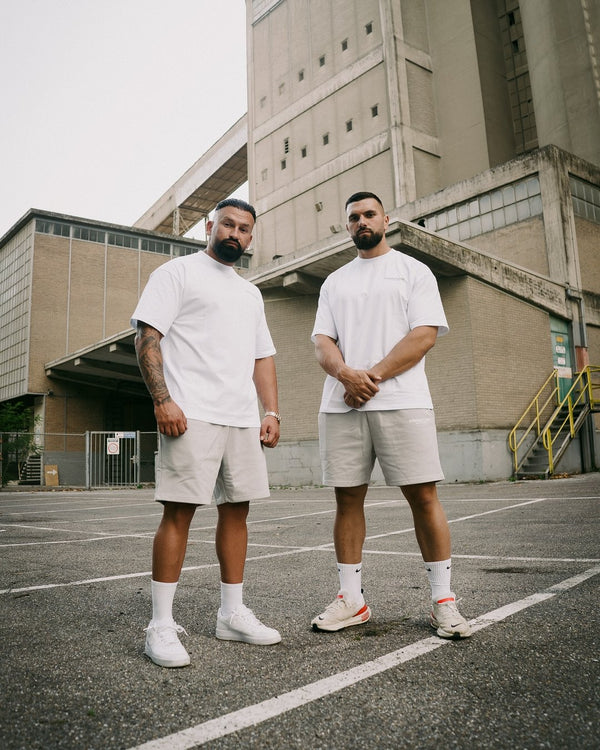 Twee mannen in witte Frontline T-shirts voor een betonnen gebouw