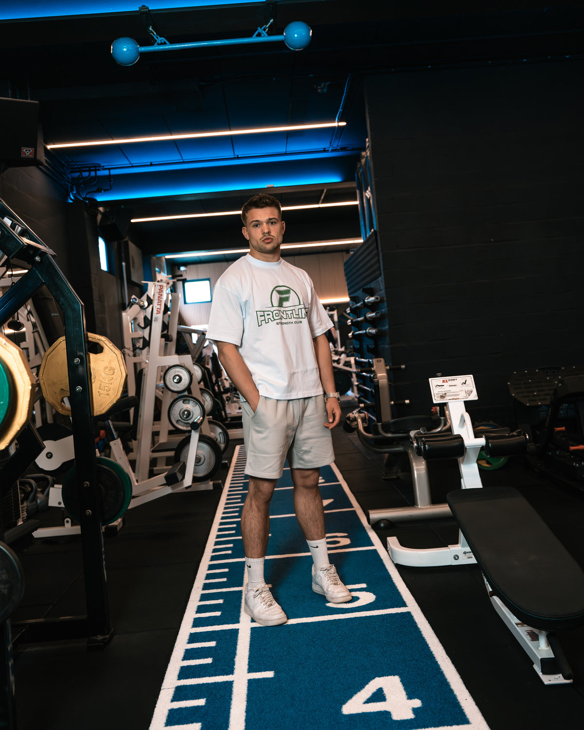Strengthclub T-Shirt wit, staand op de sprintbaan in de gym
