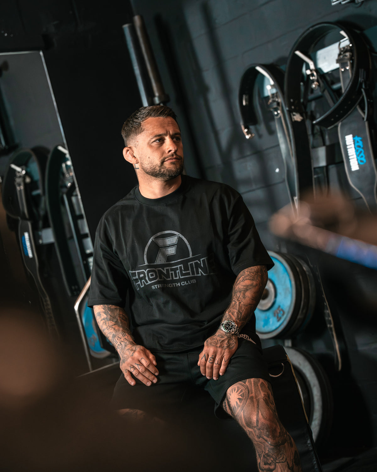 Strengthclub T-Shirt zwart, zittend in de gym bij de riemen