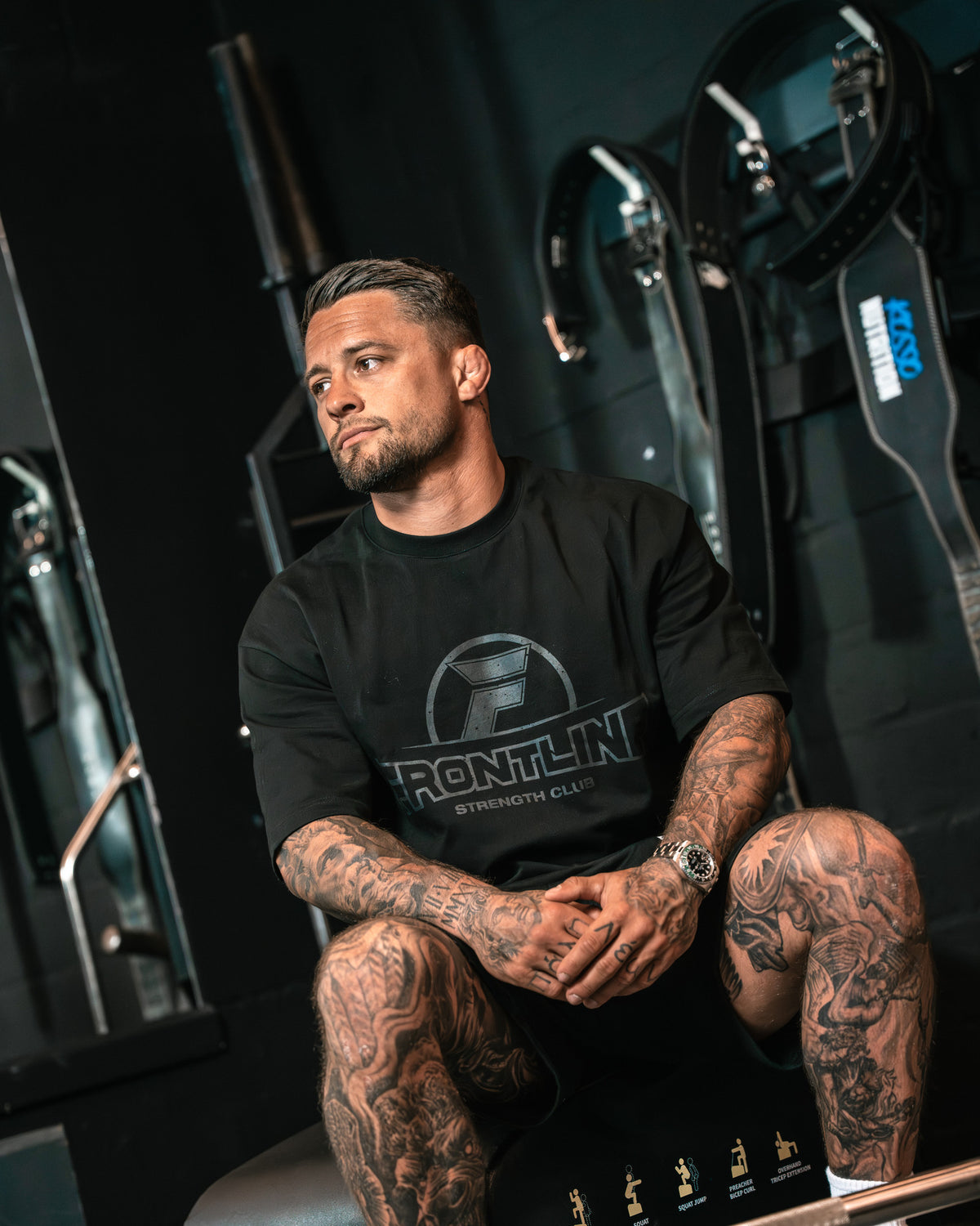 Strengthclub T-Shirt zwart, zittend op een hip thrust box