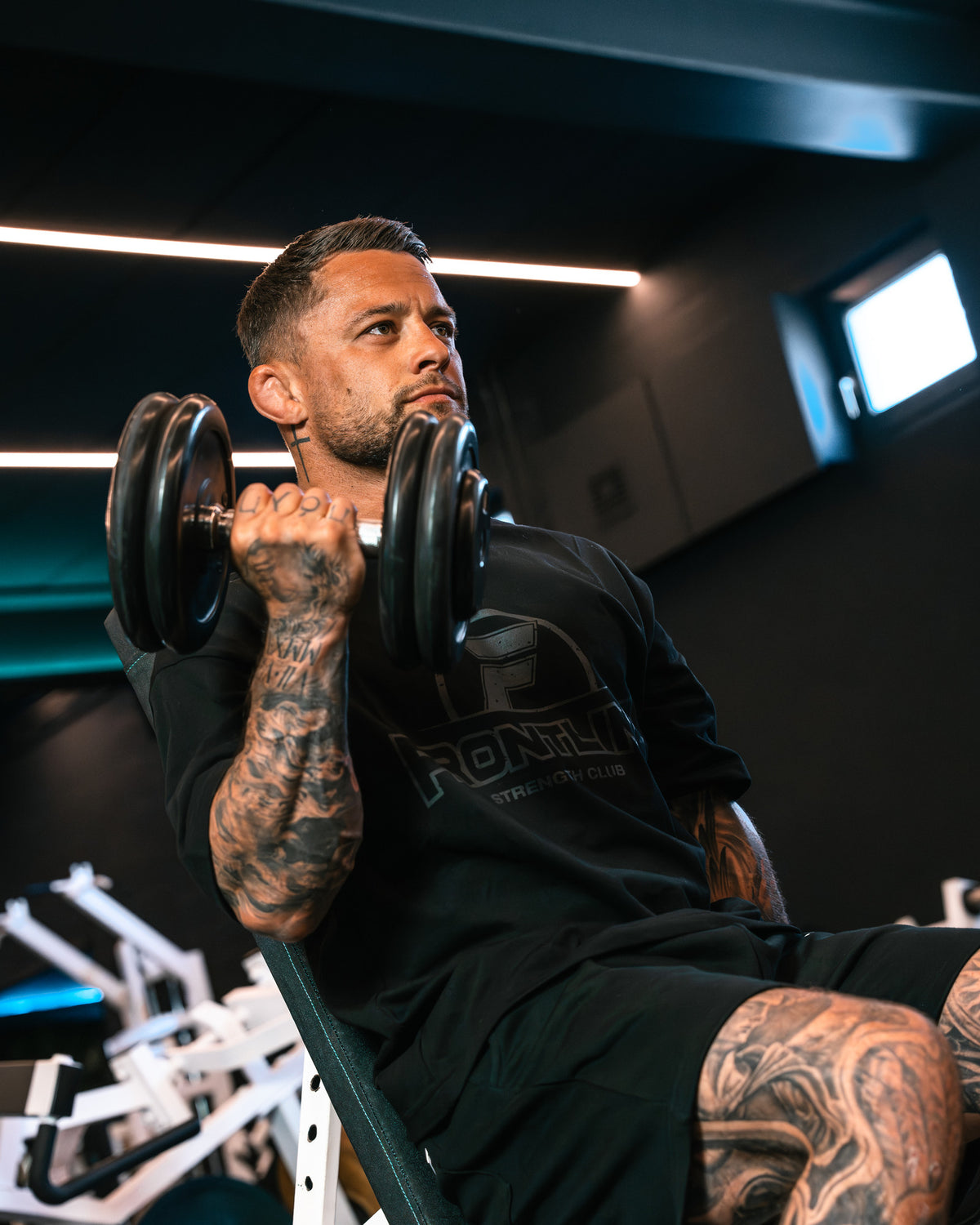 Strengthclub T-Shirt zwart tijdens een dumbbell curl