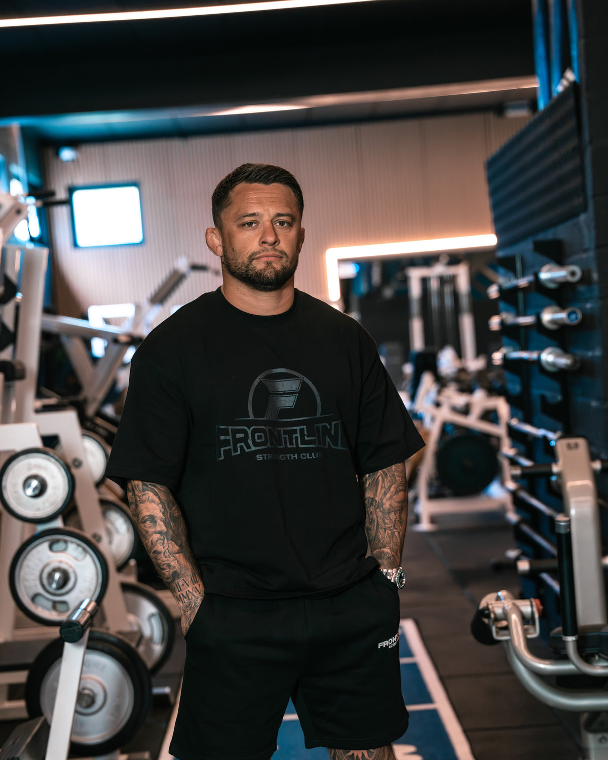 Strengthclub T-Shirt zwart, staand op de sprintbaan in de gym